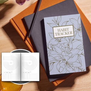 May include: A purple and white habit tracker journal with a floral design and the text "Habit Tracker" on the cover.