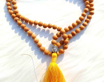 May include: A brown wooden mala bead necklace with a silver Buddha head charm and a yellow tassel.
