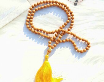 May include: A brown wooden mala bead necklace with a yellow tassel. The necklace is made of round beads and has a gold-colored accent at the top.