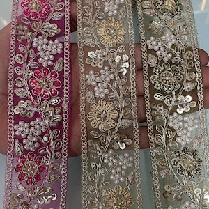 Peut inclure: Gros plan sur trois rubans décoratifs brodés. Les rubans présentent des motifs floraux avec des perles et des paillettes dorées, roses et blanches. Les rubans sont dans des tons de rose, d'or et de vert.