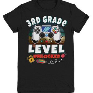 May include: Black t-shirt with a retro-style video game controller graphic. The text "3rd Grade Level Unlocked" is printed on the shirt.