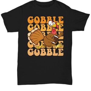 May include: Black t-shirt featuring a cartoon turkey holding a football and the word "GOBBLE" repeated in a retro font.