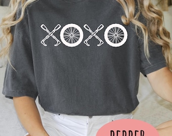 May include: Dark grey t-shirt with a white graphic design featuring the letters "XOXO" interspersed with bicycle wheels and tools. The word "PEPPER" is printed on a pink oval shape.