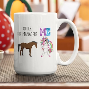 May include: White ceramic coffee mug with a graphic of a brown horse and a rainbow unicorn. The text "Other HR Managers" is above the horse and the text "ME" is above the unicorn.