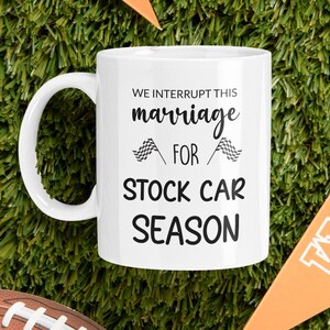 May include: White ceramic coffee mug with black text that reads "We interrupt this marriage for stock car season". The text is surrounded by two black and white checkered flags.