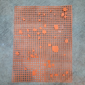 May include: A bright orange plastic canvas with a grid design and irregular cut-out shapes. The rectangular sheet is placed on a grey concrete surface. The cut-outs are of different sizes and shapes, adding a unique visual element.