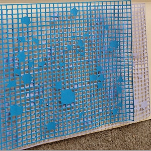 May include: A layered paper artwork with a blue grid overlay and cut-out shapes. The background features light-coloured paper with a similar grid pattern and cut-out shapes, creating a textured, dimensional effect. The artwork is on a beige background.