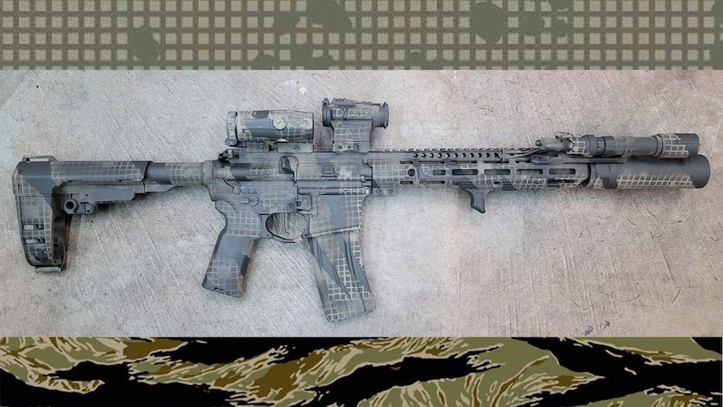 May include: A tactical rifle with a camouflage pattern in shades of grey, black, and tan. The rifle is equipped with a scope, a flashlight, and a vertical foregrip. The background is a concrete surface.