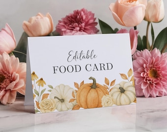 May include: A white food card with the text "Editable FOOD CARD" in black script. The card is decorated with watercolor pumpkins, leaves, and flowers in shades of orange, yellow, and white. The background features pink and peach flowers.