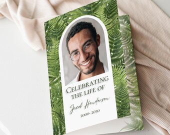 May include: A memorial card with a photo of a smiling man wearing glasses, framed by a white arch. The card is decorated with green fern leaves and the text "Celebrating the Life of Jacob Henderson 2000-2030".