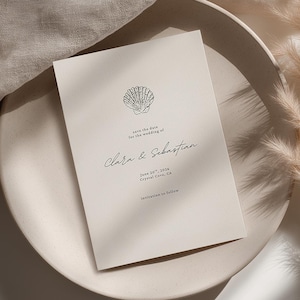 May include: A rectangular off-white wedding invitation card featuring a black line drawing of a seashell at the top, followed by the text: save the date for the wedding of Clara & Sebastian, June 24th, 2024, Crystal Cove, CA, invitation to follow.