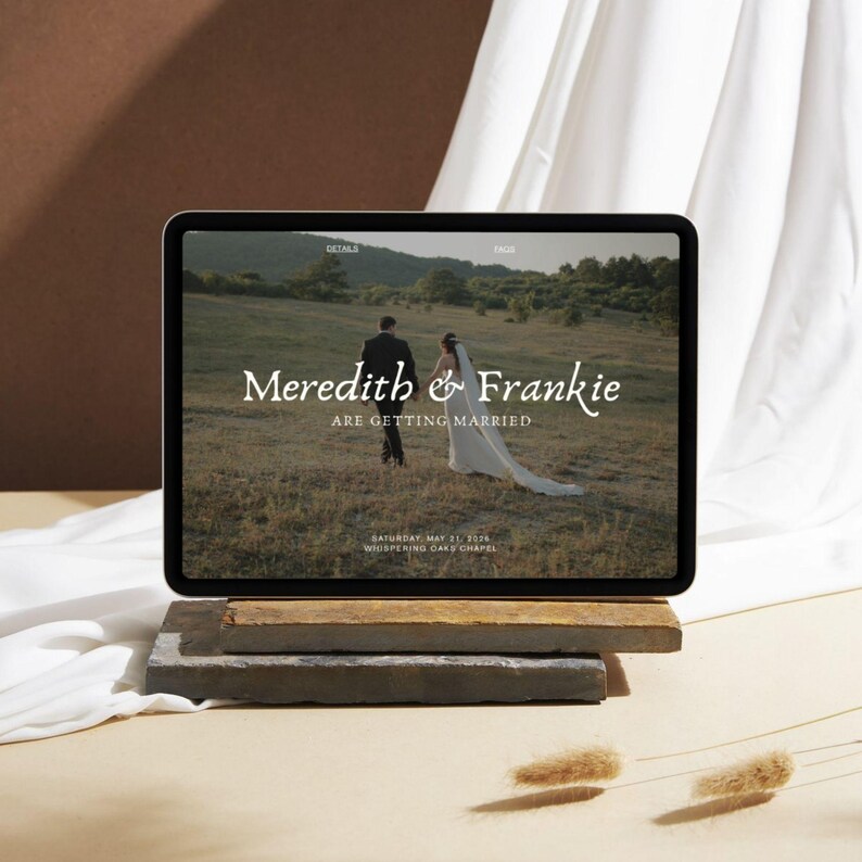 May include: A digital tablet displays a wedding announcement with the names "Meredith & Frankie" and the text "Are Getting Married." The date and location are also visible. The tablet rests on a stack of stone and wood blocks, with a neutral background.
