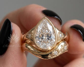 May include: A gold ring set featuring a pear-shaped centre stone in a bezel setting, accompanied by a curved band. Both pieces are decorated with small star-shaped engravings and tiny inset diamonds, creating a celestial-inspired design.