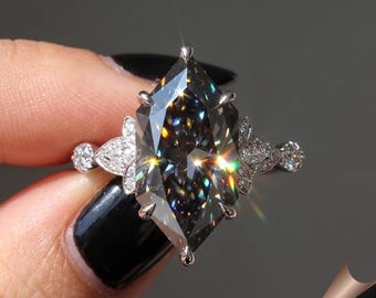 May include: A silver engagement ring featuring a large, gray, shield-cut gemstone. The ring has a floral design with smaller, clear stones on the band and around the main stone. The gemstone reflects multiple colors.