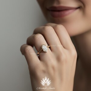 May include: A gold ring with a unique, geometric, white gemstone. The ring's design features a hexagonal stone set within a thin gold band. The ring is on a person's finger. The brand name "Aerokefe Jewels" is visible in the image.