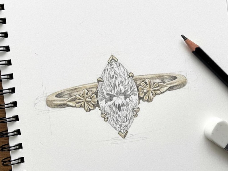 Puede incluir: Boceto a l&aacute;piz de un anillo de compromiso con un diamante talla marquesa. El anillo tiene una banda dorada con detalles florales a cada lado del diamante. Un l&aacute;piz y una goma de borrar est&aacute;n en el fondo.