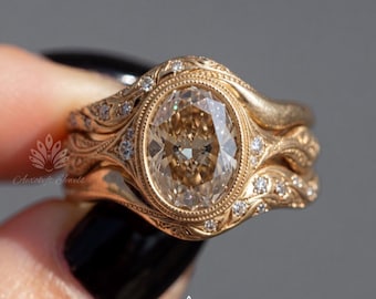 May include: A gold ring set featuring a central oval-cut champagne-colored gemstone in a bezel setting, surrounded by a decorative band with intricate engravings and small round accent stones embedded along the sides of the metal shank.