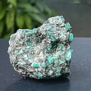 Peut inclure: Une pierre d'émeraude brute et non taillée, avec une matrice gris foncé. Les cristaux d'émeraude sont d'un vert vif, contrastant avec les tons gris et argentés de la roche environnante. La pierre a un aspect naturel et non poli.