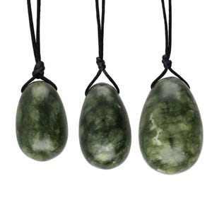 May include: Three green jade egg pendants with black cords. The eggs vary slightly in size and have a mottled appearance with darker green veining. The cords are knotted at the top for hanging.