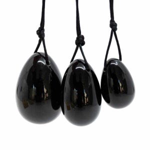 May include: Three black, polished, egg-shaped stones suspended by black cords. The stones have a glossy finish and are of varying sizes. The cords are knotted at the top, suggesting they can be hung or worn.