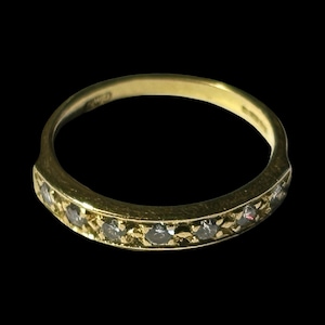May include: A gold band ring with a row of small, clear gemstones set along the top. The ring has a smooth, polished finish and a classic design. The ring is set against a black background.