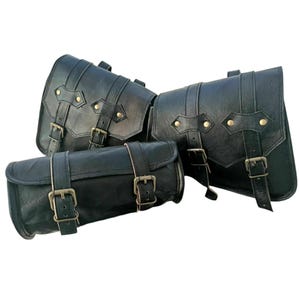 May include: Three black leather motorcycle saddlebags and a tool bag. The bags have a classic design with buckles and straps. The bags are made of a durable leather material and are designed to be mounted on a motorcycle.