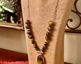 May include: A gold chain necklace with a large oval tiger's eye pendant and brown tiger's eye beads.