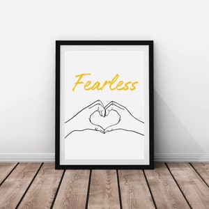 May include: Black framed print with a white background. The print features a hand drawn image of two hands forming a heart shape. The word "Fearless" is written in yellow above the hands.