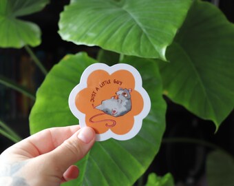 May include: A sticker with a flower-shaped outline and an orange background. The sticker features a cartoon illustration of a gray mouse with the text "Just a little guy" in red.