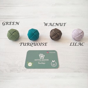 Pode incluir: Quatro botões redondos tecidos em verde, turquesa, marrom e lilás. Os botões são etiquetados com suas cores: verde, turquesa, noz e lilás. O texto "RATTAN SANDIK Home Design" é visível em um pequeno cartão abaixo dos botões.