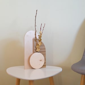 May include: A wooden vase with a geometric design in shades of brown and beige. The vase is filled with dried branches and leaves.