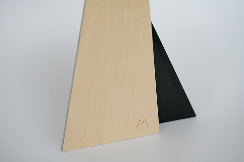 K&ouml;nnte beinhalten: Ein Holzdreieck mit einem schwarzen Dreieck oben drauf. Das Holzdreieck hat die Buchstaben "A M" eingraviert.