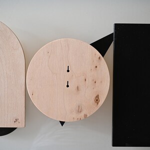 K&ouml;nnte beinhalten: Ein Set aus drei Wandobjekten, bestehend aus einem Bogen aus hellem Holz, einem Kreis aus hellem Holz und einer schwarzen rechteckigen Platte. Jedes Teil hat zwei vertikale Schl&uuml;ssellochschlitze zur Montage und zeigt nat&uuml;rliche Maserungen.