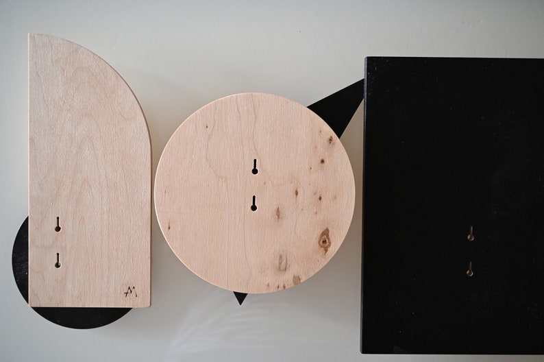 K&ouml;nnte beinhalten: Ein Set aus drei Wandobjekten, bestehend aus einem Bogen aus hellem Holz, einem Kreis aus hellem Holz und einer schwarzen rechteckigen Platte. Jedes Teil hat zwei vertikale Schl&uuml;ssellochschlitze zur Montage und zeigt nat&uuml;rliche Maserungen.