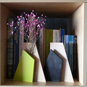 K&ouml;nnte beinhalten: Ein Satz aus drei Holzbuchst&uuml;tzen in Form von Bergen. Die Buchst&uuml;tzen sind in Beige-, Gr&uuml;n- und Schwarzt&ouml;nen lackiert. Die Buchst&uuml;tzen stehen in einem B&uuml;cherregal mit einer Auswahl an B&uuml;chern und einer Vase mit rosa Blumen.