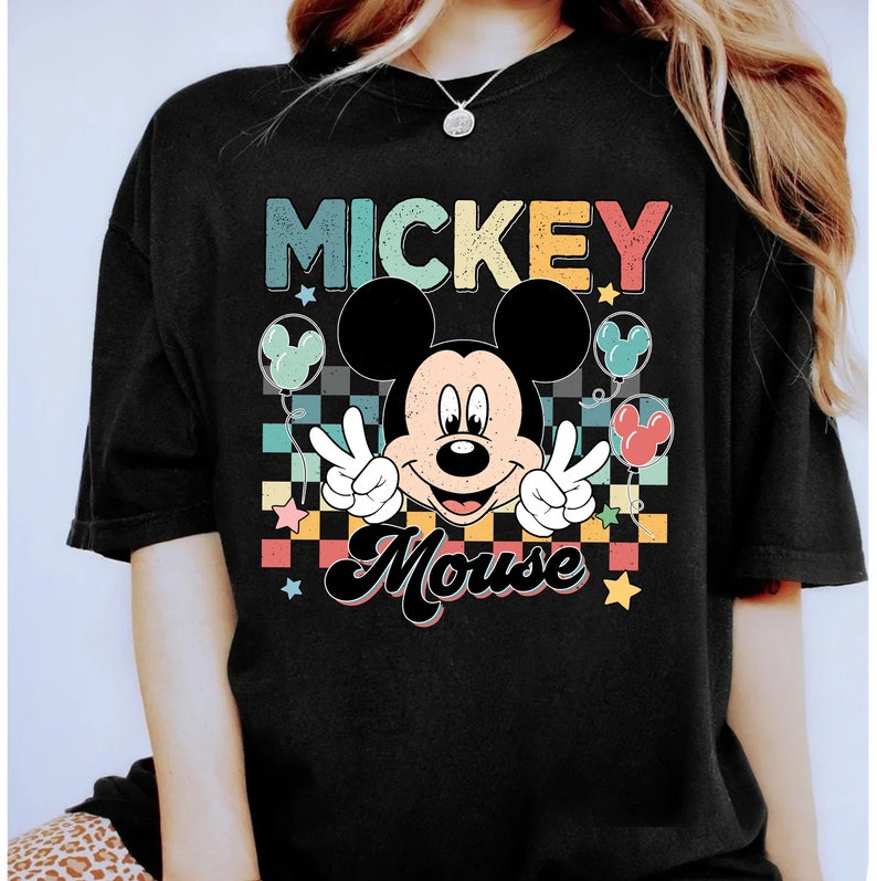 K&ouml;nnte beinhalten: Schwarzes T-Shirt mit einer Retro-Grafik von Mickey Mouse mit dem Text "Mickey Mouse" in Regenbogenfarben.