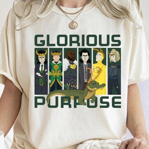 Puede incluir: Camiseta color crema con un gráfico de seis personajes de dibujos animados y un caimán verde. El texto "GLORIOUS PURPOSE" está impreso en letras verdes en bloque encima y debajo de los personajes.