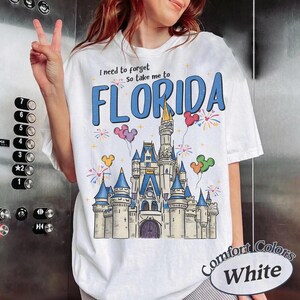 May include: White t-shirt with a castle graphic and the word "FLORIDA" in blue. The shirt also features the text "I need to forget, so take me to". The shirt is a Comfort Colors brand.