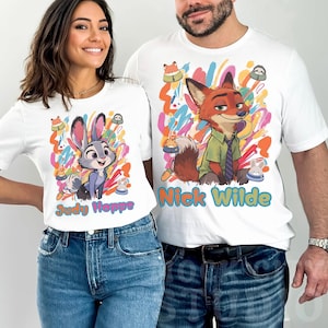 May include: White t-shirts with cartoon characters Judy Hopps and Nick Wilde from Zootropolis. The shirts have colourful abstract backgrounds and character names. The woman is wearing a shirt with Judy Hopps, and the man is wearing a shirt with Nick Wilde.