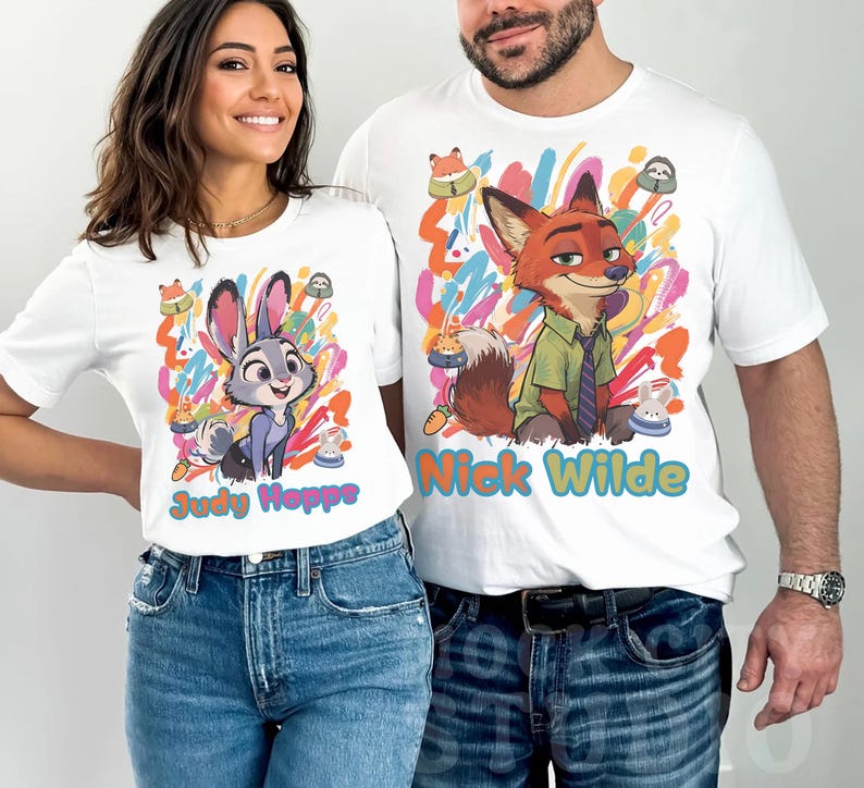May include: White t-shirts with cartoon characters Judy Hopps and Nick Wilde from Zootropolis. The shirts have colourful abstract backgrounds and character names. The woman is wearing a shirt with Judy Hopps, and the man is wearing a shirt with Nick Wilde.