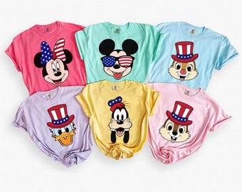 Può includere: Sei magliette colorate con personaggi Disney. Ogni maglietta mostra un personaggio diverso, tra cui Minnie Mouse, Topolino, Paperino, Pippo e Cip e Ciop, tutti con disegni patriottici. Le magliette sono in vari colori come rosa, blu e giallo.