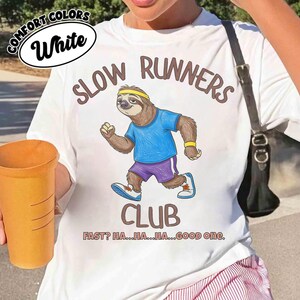 May include: White t-shirt with a cartoon sloth running, wearing a blue shirt and purple shorts. The text reads "SLOW RUNNERS CLUB" with the phrase "FAST? HA...HA...HA...GOOD one." The shirt also has the words "COMFORT COLORS" and "White".