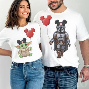 May include: White t-shirts with cartoon characters. One shirt shows a green alien holding a red Mickey Mouse balloon. The other shows a character in silver armour holding a red Mickey Mouse balloon. Both characters wear Mickey Mouse hats.