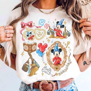 Könnte beinhalten: Cremefarbenes T-Shirt mit einem skurrilen Design mit Mickey Mouse in einem Zaubererhut und -robe. Das Design umfasst Herzen, Feuerwerk, Bücher, Luftballons und den Text "Some Imagination Huh?" und "Fantastic".