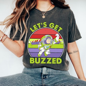 May include: A black t-shirt with a vintage-style graphic of Buzz Lightyear from Toy Story. The graphic features a red, orange, yellow, and purple sunset with the text "Let's Get Buzzed".