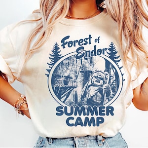 May include: Cream-colored sweatshirt with a blue graphic. The graphic features the text "Forest of Endor SUMMER CAMP" in a circular design with a forest scene and a character. The sweatshirt has long sleeves.