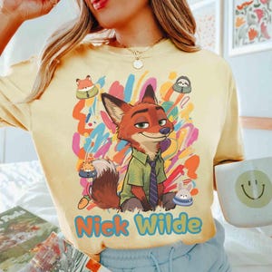 May include: Yellow t-shirt with a cartoon image of Nick Wilde from Zootropolis. The design shows Nick in a green shirt and tie, with colourful abstract art and the name "Nick Wilde" in blue.