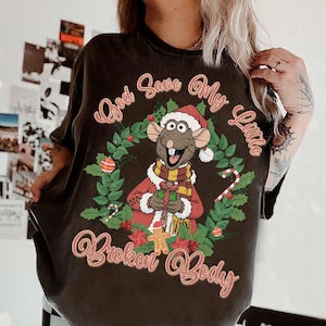 May include: Dark gray t-shirt featuring a cartoon rat wearing a Santa hat and scarf, holding a gift, surrounded by a Christmas wreath. The text "God Save My Little Broken Body" is arched around the design.