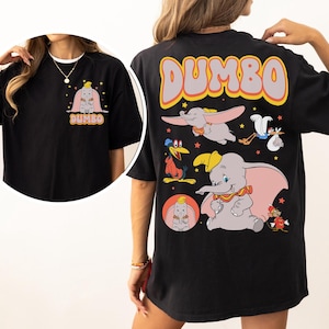 May include: Black t-shirt featuring Dumbo the elephant. The front has a small graphic of Dumbo, and the back has a larger design with Dumbo and other characters. The word "Dumbo" is in large letters across the top.