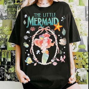 以下が含まれることがあります： 黒いTシャツ。映画「リトル・マーメイド」のアリエルのカラフルなイラストが特徴です。「The Little Mermaid」の文字がターコイズと白で描かれ、ヒトデ、真珠、その他の海の生き物が描かれています。カジュアルでオーバーサイズのフィット感です。
